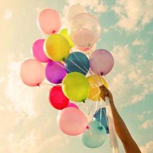 Hand holding a bunch of colorful balloons against a bright sky