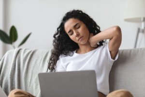 Brunette woman having pain in neck while working with laptop patient holding their neck in pain